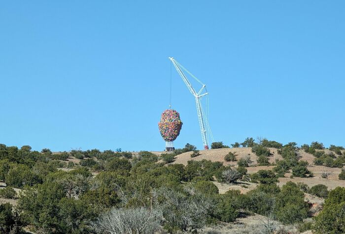 Crane lifting a colorful, oversized balloon cluster in a landscape, capturing a unique sight few would believe without a photo.