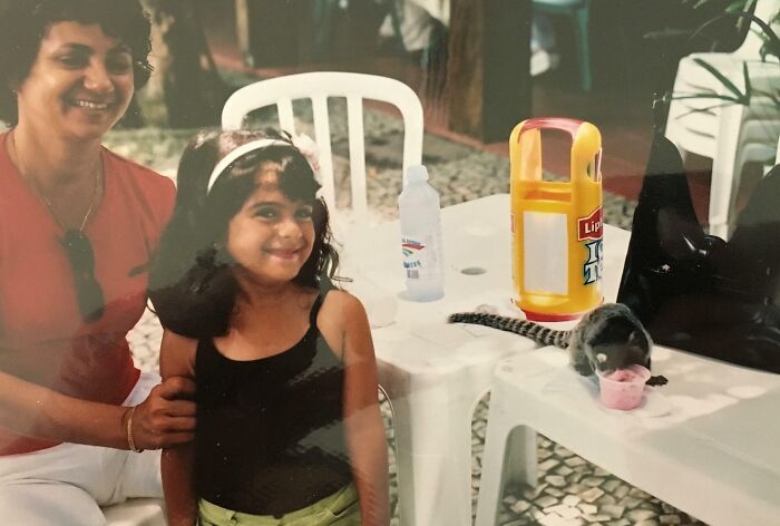 A joyful girl next to a curious animal drinking from a cup, capturing an unbelievable moment.