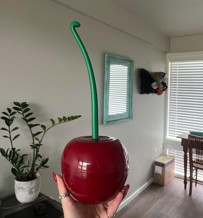 A hand holding a cherry-shaped cup with a long green straw, featuring unusual home décor.