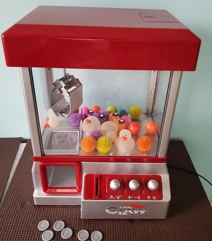 Red toy claw machine with colorful balls and ducks, encapsulating a weird find.