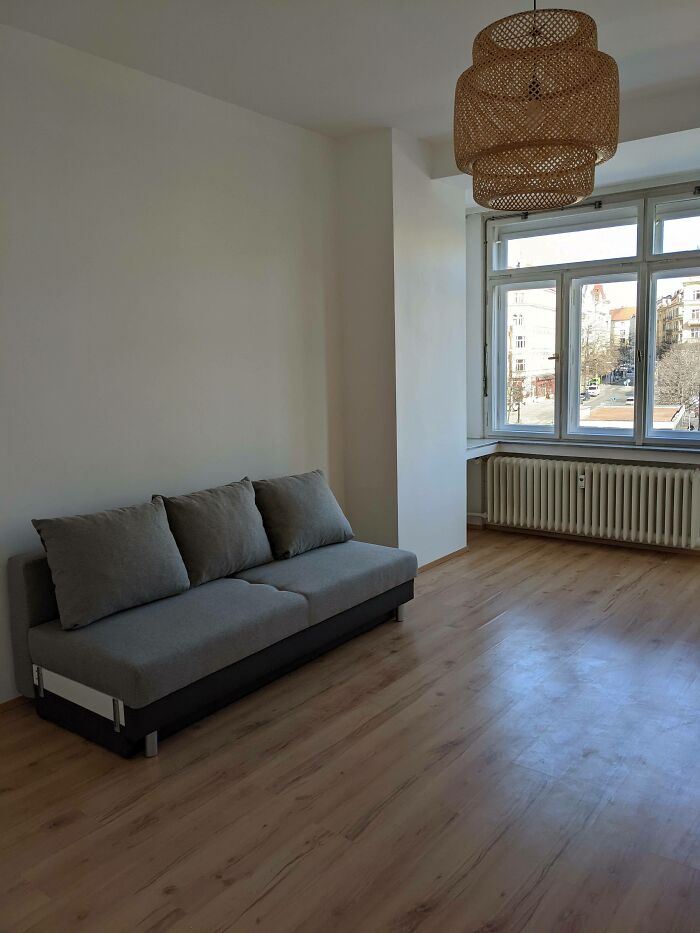 Minimalist living room with gray sofa, wooden flooring, large window, and a woven hanging light fixture, interior design trends.