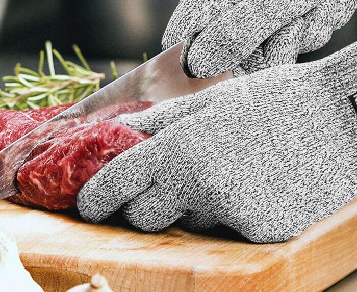 Cut-resistant gloves slicing meat with a sharp knife on a wooden board.