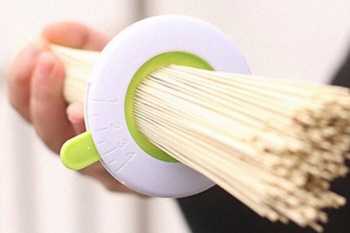 Hand holds spaghetti measurer, a useful tool for portioning uncooked pasta accurately.