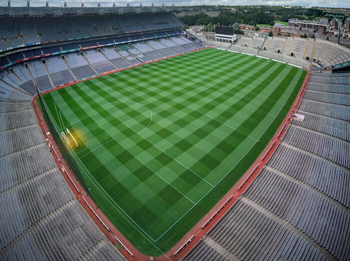 Aerial view of a large soccer stadium with empty seats and a checkered green pitch, a cathedral of soccer.