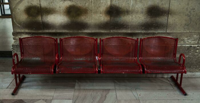Aged red metal bench with wear marks on a wall, showing transformation by time and use.
