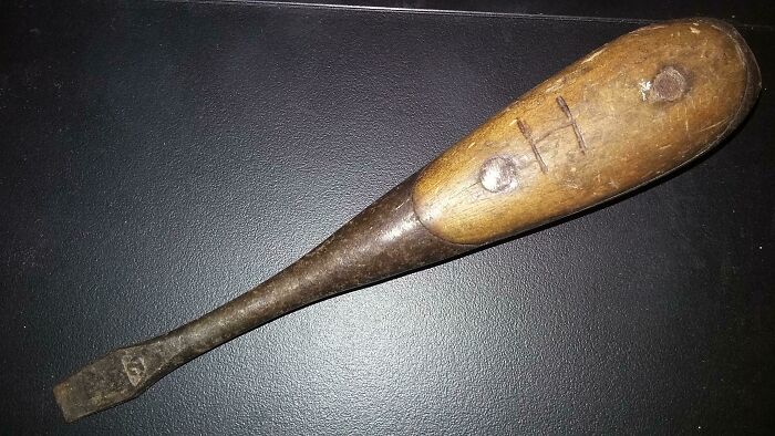 Aged wooden tool with handle showing signs of transformation by time and use, on a dark surface.