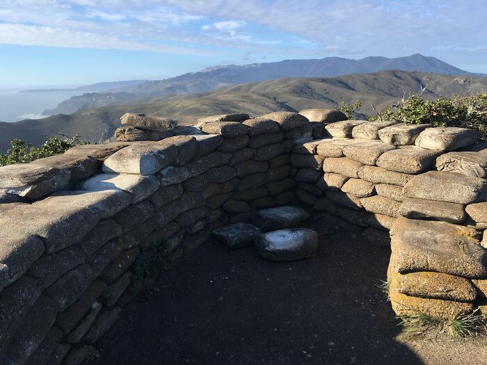 Stone wall overlooking scenic, grassy mountains transformed by time, with blue sky and distant peaks.