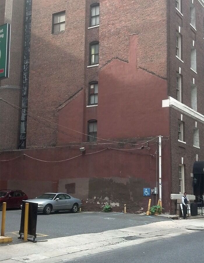 Unused parking area beside a brick building, showing the faded outline of a removed building, transformed by time and use.