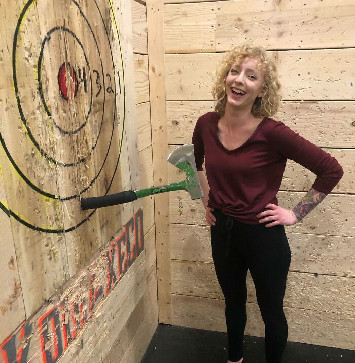 Smiling woman poses by an axe stuck in a bullseye target, capturing an incredible moment.