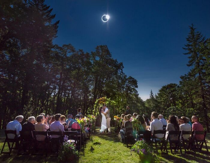 Wedding ceremony taking place during solar eclipse, with guests seated outdoors under a clear sky.