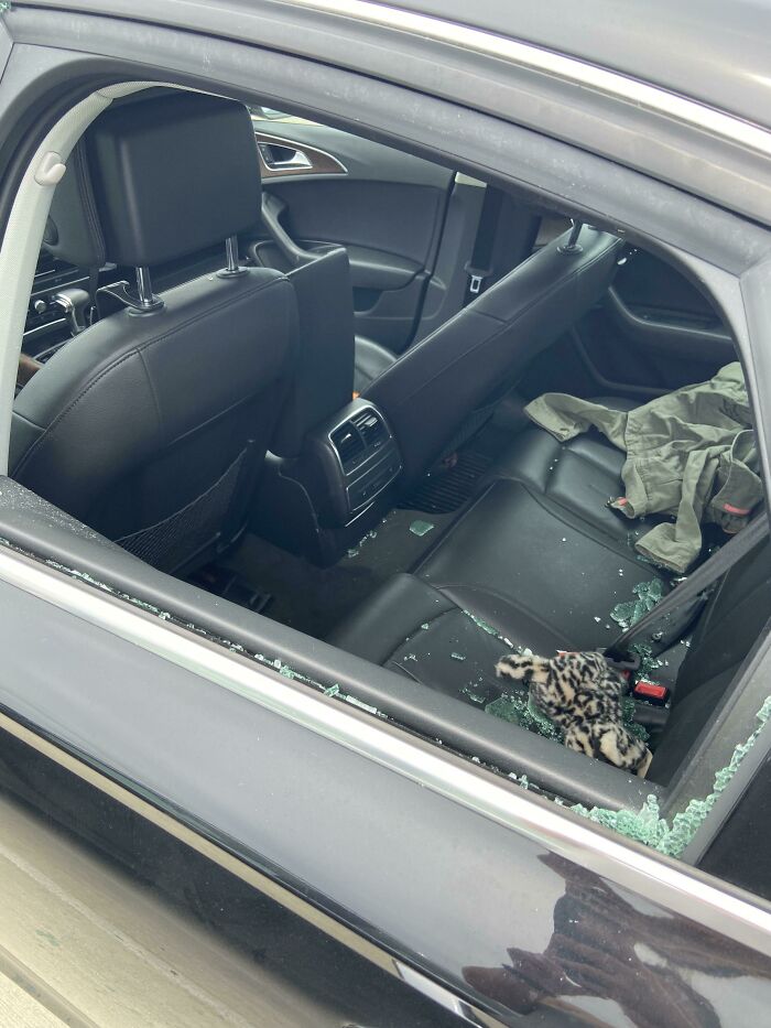 Car with shattered window, glass on seats, reflecting a horrible day scenario.