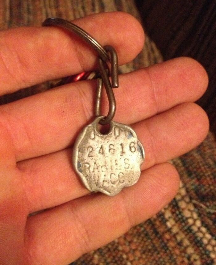 Worn metal tag in hand, showing effects of time and use, engraved with numbers and letters.