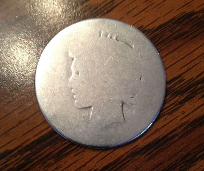 Worn coin with faint silhouette on wooden surface, exemplifying time's transformative effects.