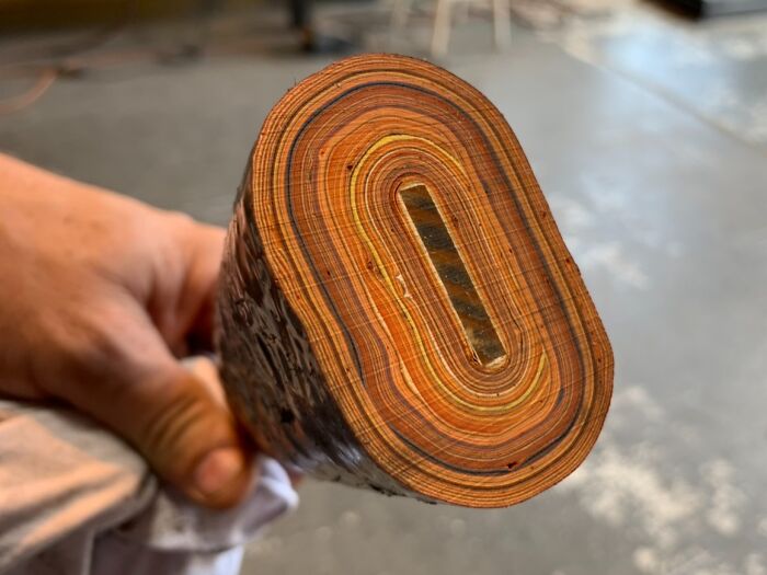 Close-up of a hand holding a well-worn hockey stick, showing layers of wood transformed by time and use.