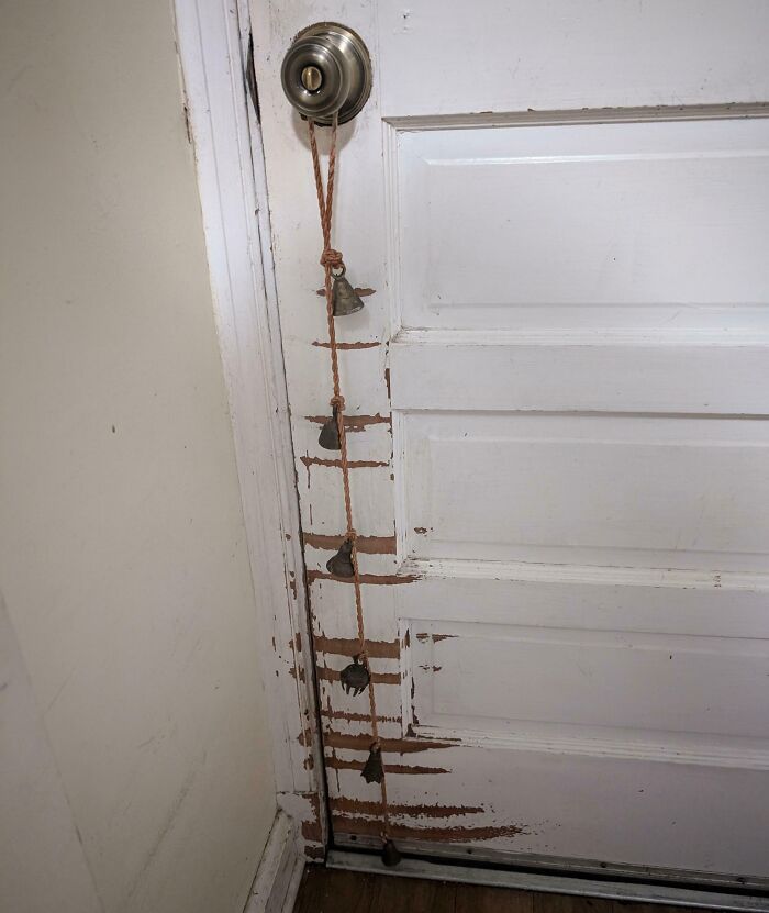 A door with a rope of bells and visible wear, showing the effects of time and use on the paint.