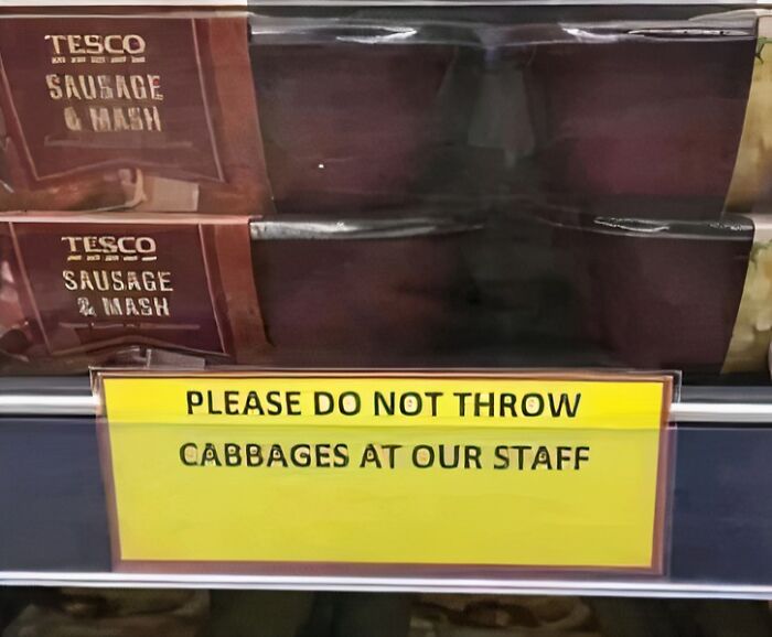 Store sign humorously asking not to throw cabbages at staff, placed near sausage and mash display.