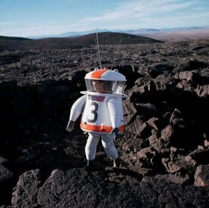 Astronaut training during the JFK years, wearing a unique space suit in a rocky landscape.