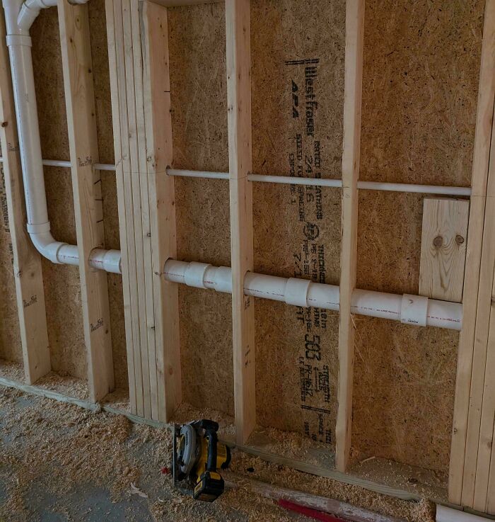 Exposed construction wall with improperly installed pipes, showcasing dangerous building conditions.