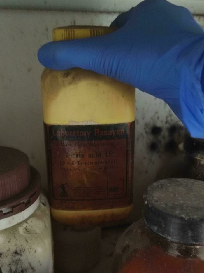 Persona con guante azul sostiene frasco de ácido en laboratorio, sin darse cuenta del peligro.