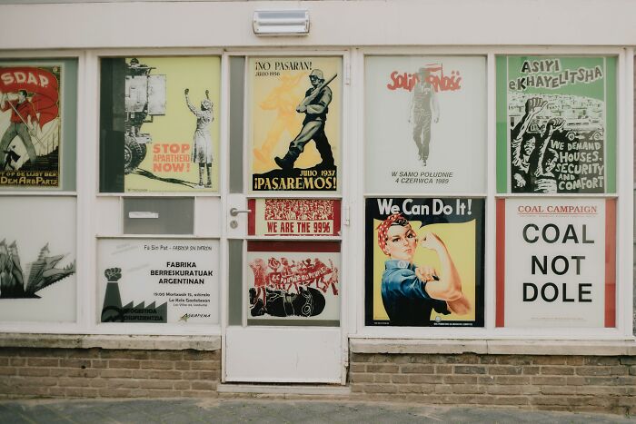Collection of vintage posters in a display window, featuring various slogans and historical images.