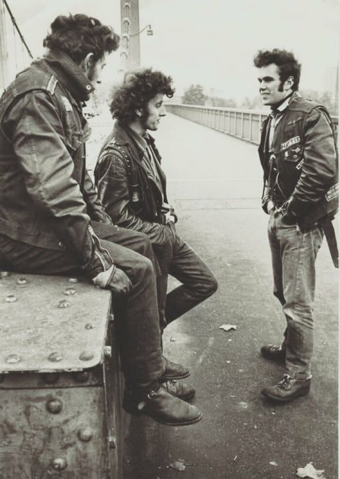 Motorcyclists in leather jackets chatting on a bridge, capturing a lesser-known historical moment.