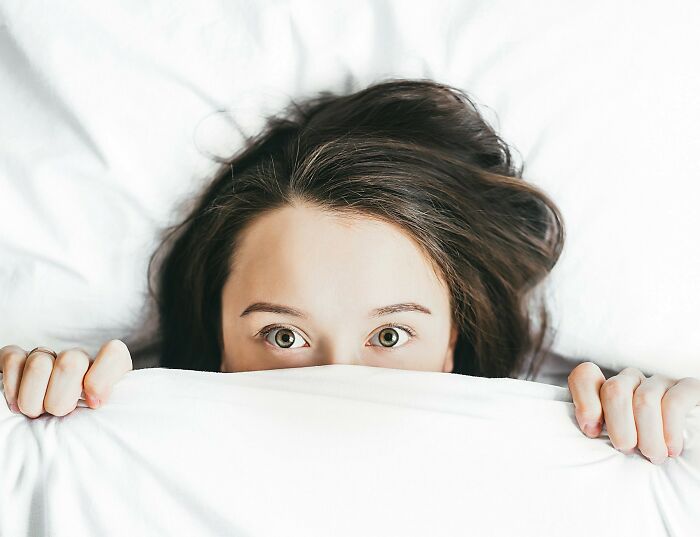 A woman in bed looking surprised under a white sheet, highlighting sudden dizziness awareness.