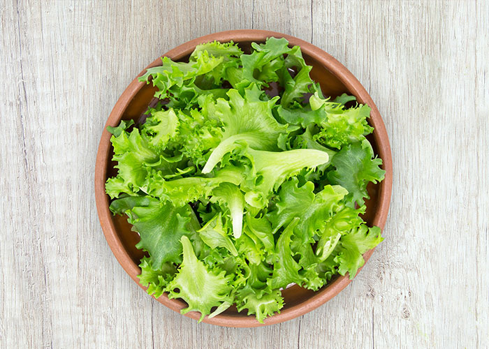 A bowl of fresh green lettuce on a wooden table, illustrating once exotic foods.