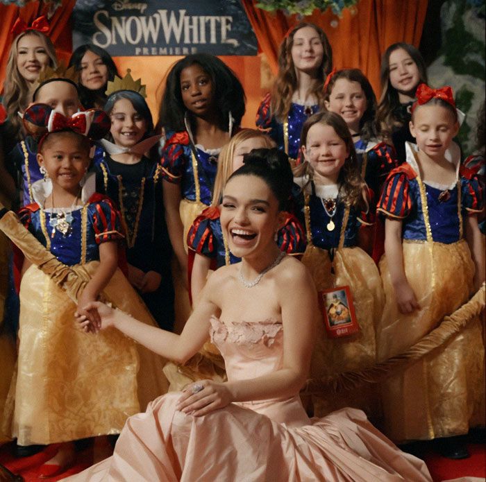 Smiling woman in a pink dress at 'Snow White' premiere with children dressed as characters.