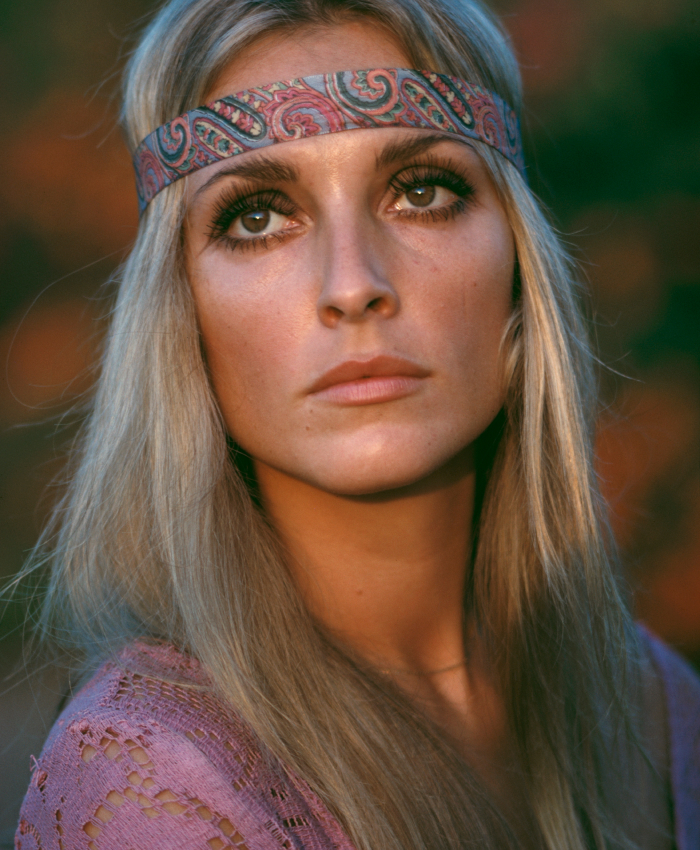 A woman with long blonde hair and a patterned headband gazes upward, wearing a knitted purple top.