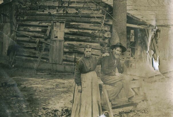 Historical photo of a man and woman outside a rustic log cabin, offering a glimpse into the past.