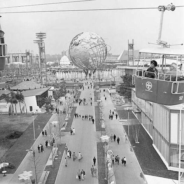 Historical photo of people exploring the World's Fair with a large globe sculpture in the background, enhancing past perspective.