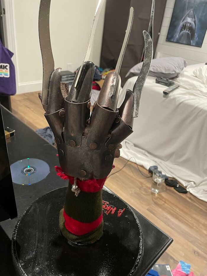 A replica of a metal glove with blades, a popular movie prop, displayed on a stand in a room setting.