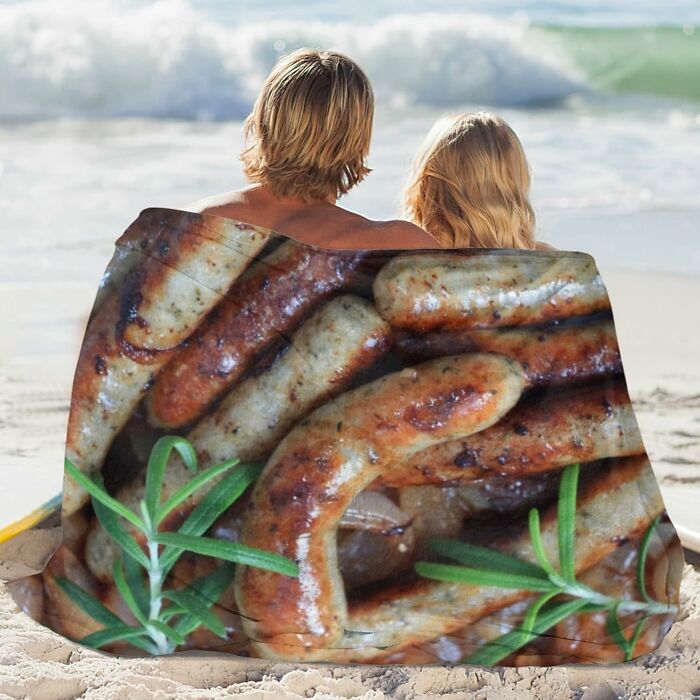 Couple sitting on beach wrapped in blanket with sausage print, an amusing Amazon find.
