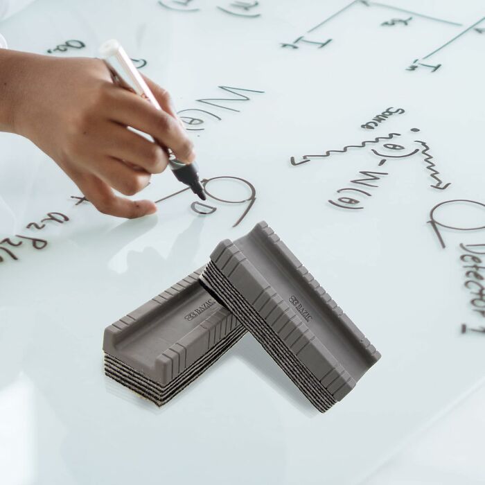 Hand writing equations on glass with erasers nearby, showcasing extraordinary educational tools.