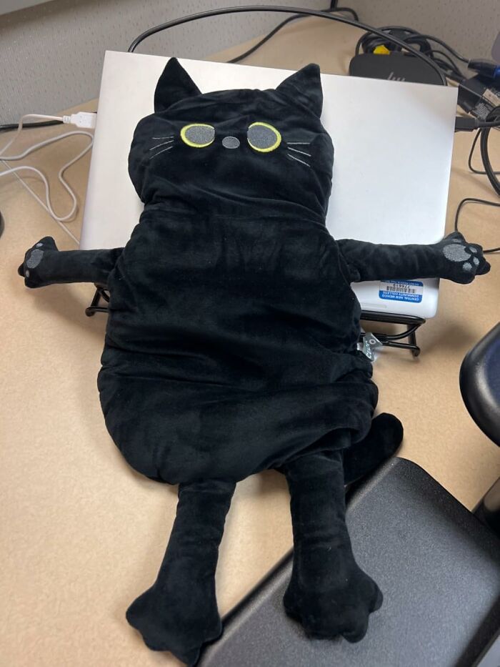 A black cat pillow stretched on a laptop, offering a cheap fix for laptop heat management issues.