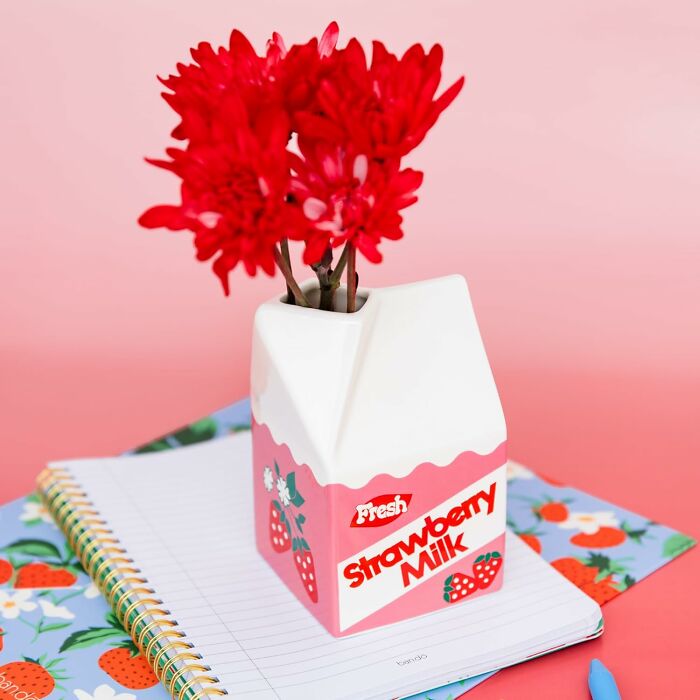 Carton-shaped vase with red flowers, styled like strawberry milk on a notebook with strawberry motifs.