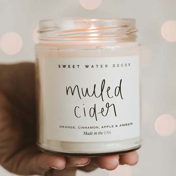 A hand holding a small business product candle labeled "Mulled Cider" by Sweet Water Decor.