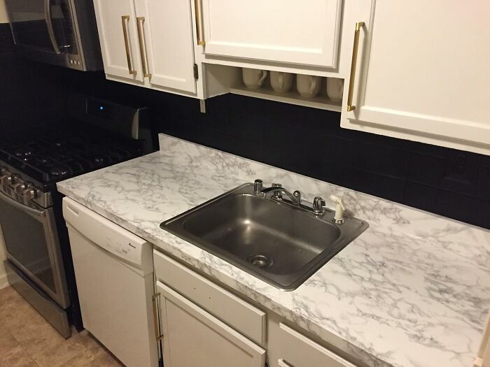 DIY home project: Marble-patterned kitchen countertop transformation with white cabinets and stainless steel sink.