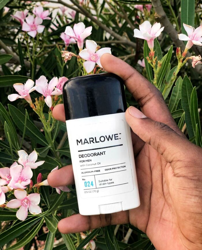 Hand holding Marlowe deodorant, a small business product on Amazon, in front of pink flowers.