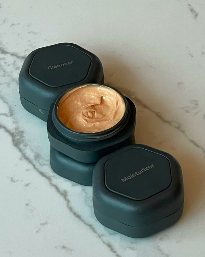 Two black containers labeled Cleanser and Moisturizer on a marble surface.