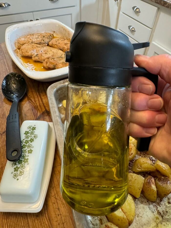 A hand holding an oil dispenser in a kitchen with cooked chicken and potatoes, highlighting Costco a*******n management.