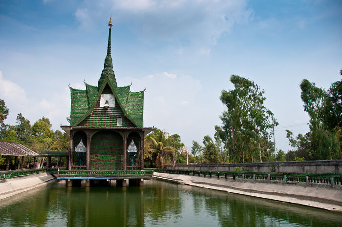 Iconic green temple above water, surrounded by trees under a blue sky.