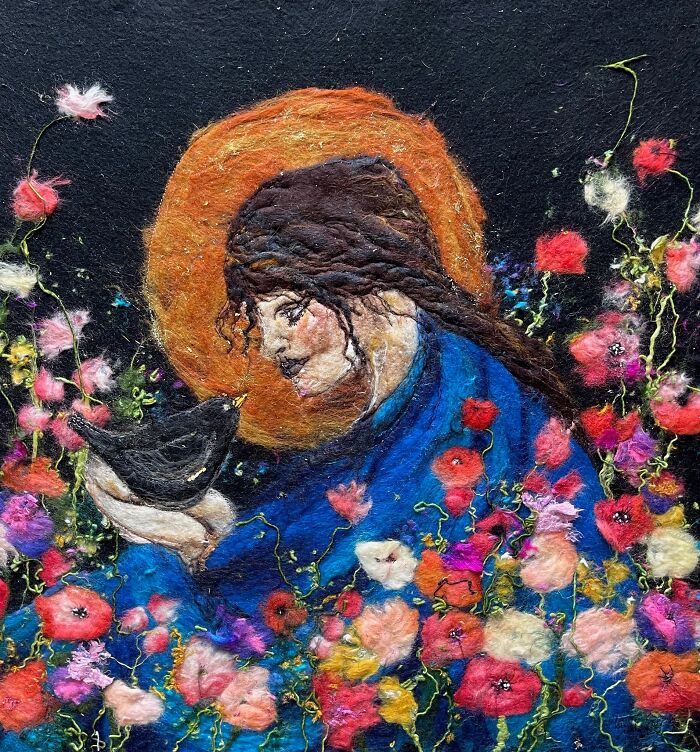 Fiber artwork of a woman holding a blackbird, surrounded by colorful flowers, showcasing beautiful scenery.