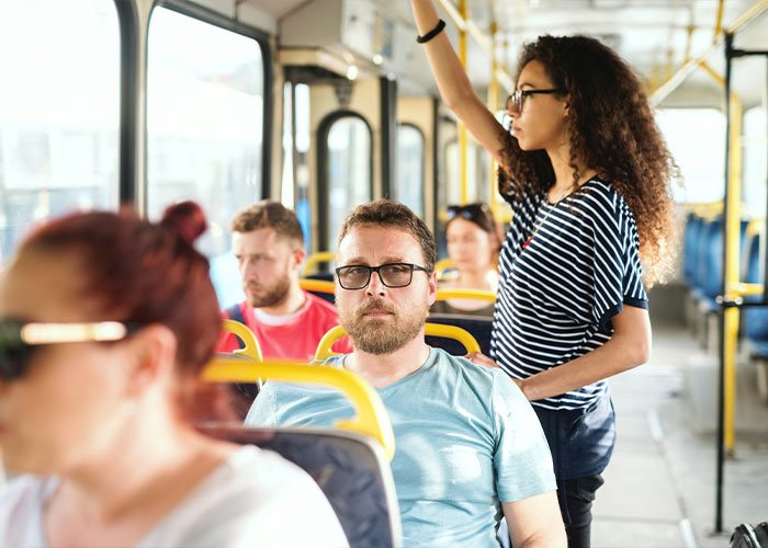 A man with glasses on a bus, appearing thoughtful, surrounded by other passengers, illustrating "trashy parent" behaviors.