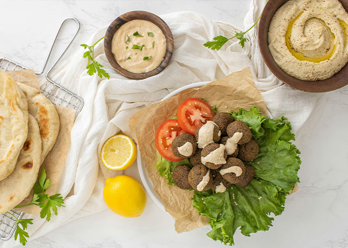 Exotic foods: falafel, hummus, flatbread, tomatoes, and lemon on a white table setting.