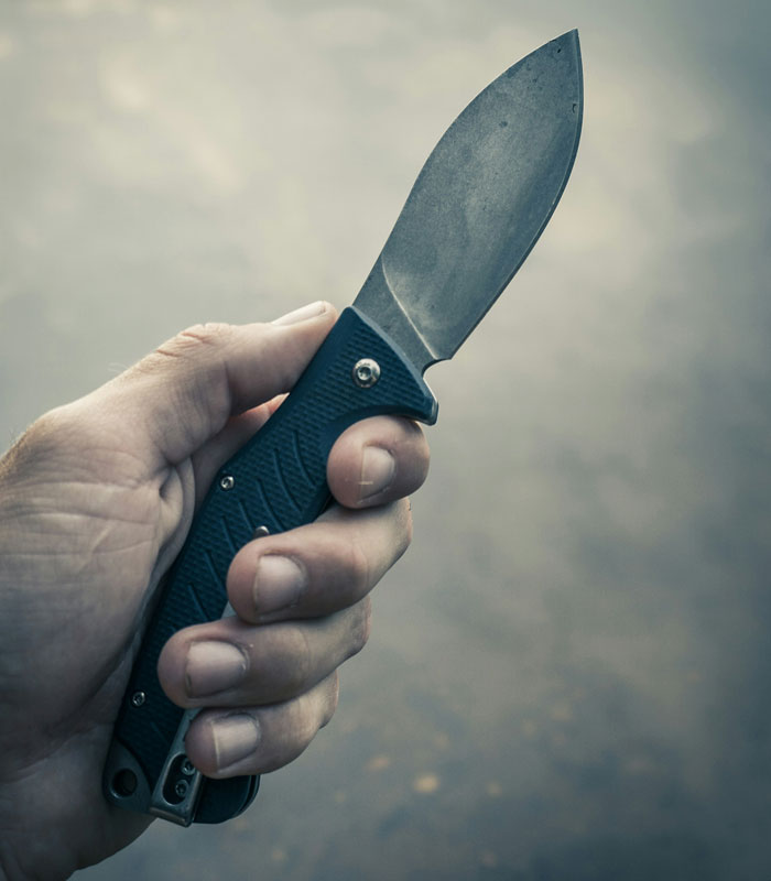 A hand holding a black survival knife with a sharp blade, essential for life-saving situations.