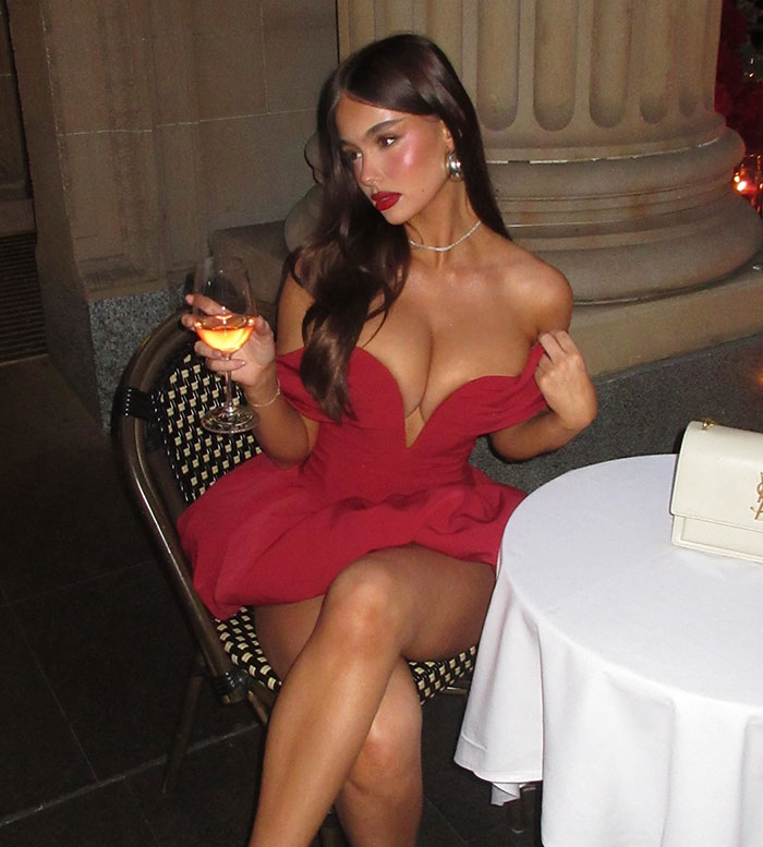 Model in a red dress at a wedding, holding a drink, with controversy over outfit choice.