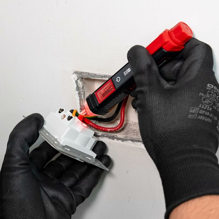 Gloved hands using a voltage tester on exposed wires. Contractor inspection and safety check.