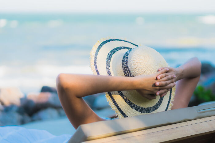 Person relaxing on a beach chair with a hat, embodying workplace revenge by taking an unplanned day off.