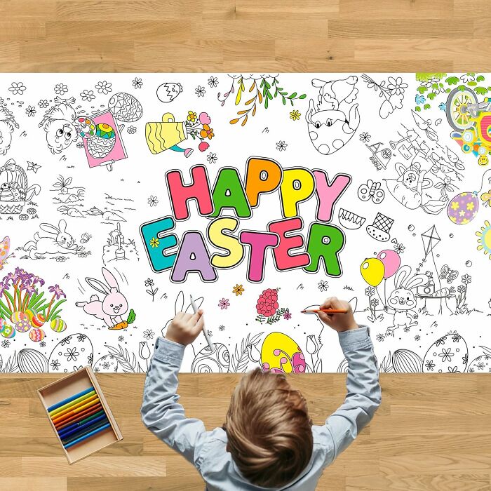 Child coloring a large "Happy Easter" poster with vibrant designs, surrounded by coloring pencils on a wooden floor.